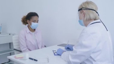 Koruyucu kalkan doktoru hastayı muayene ediyor, hastalık salgınını önlüyor.