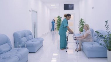 Bakım hemşiresi, hastaya koridorda Walker 'la taşınması ve rehabilitasyonu için yardım ediyor.