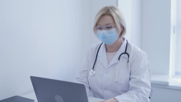 Consultant médical en masque de protection travaillant sur ordinateur portable, diagnostics en ligne — Video