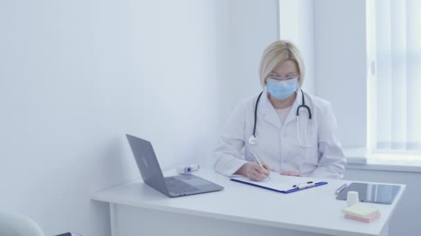 Thérapeute féminine écrivant des antécédents médicaux, assise à table à la clinique, au travail — Video