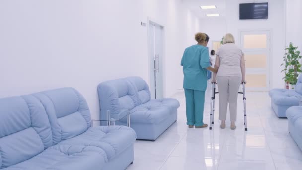 Hemşire, kadın hastaya klinikte yürüyen travmatoloji ünitesinde yardım ediyor. — Stok video