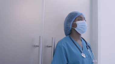 Yorgun Afro-Amerikalı stajyer hastane koridorunda tek başına duruyor, aşırı çalışma stresi