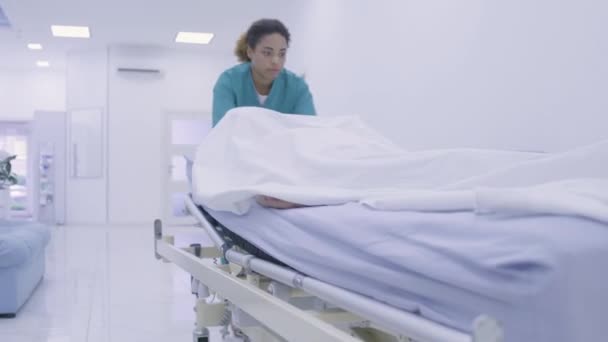 Enfermera negra transportando cadáver en la sala del hospital, mano colgando de la camilla — Vídeo de stock