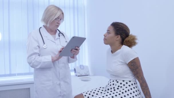 Arts die patiënt in kliniek vult medische dossiers op tabblad, vrouwelijke gezondheid — Stockvideo