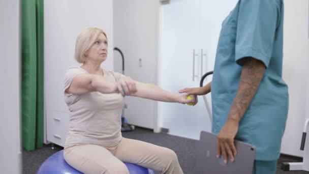 Señora mayor haciendo ejercicios de recuperación muscular en el gimnasio, médico de apoyo paciente — Vídeo de stock