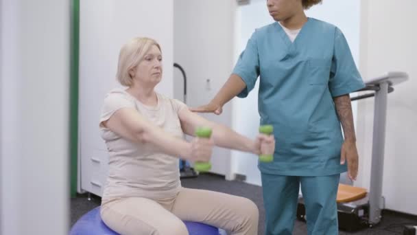 Señora mayor que está tomando terapia de rehabilitación en la clínica, haciendo ejercicio bajo el control del médico — Vídeo de stock