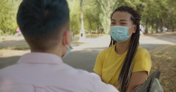 Female friends in protective masks talking, sitting on the bench in park, virus — Stock Video