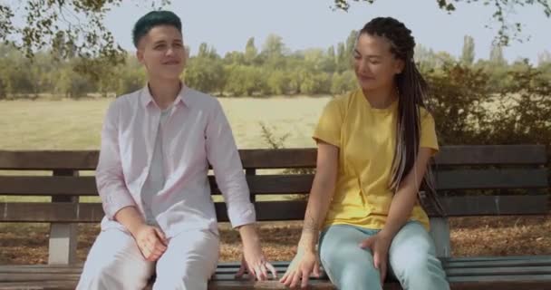 Ευτυχισμένο λεσβιακό ζευγάρι που κρατιέται χέρι χέρι, κάθεται στον πάγκο στο πάρκο, πρώτο ραντεβού — Αρχείο Βίντεο