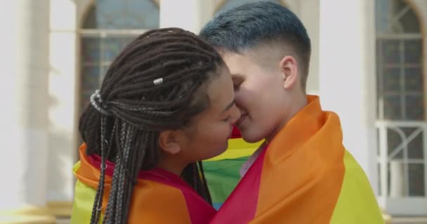 Νεαρές γυναίκες που φιλιούνται, καλυμμένες με σημαία ουράνιου τόξου, σχέσεις μεταξύ ατόμων του ιδίου φύλου, δικαιώματα Igbt — Αρχείο Βίντεο