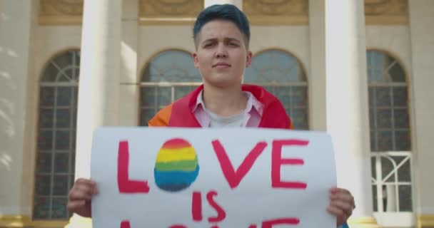 Gay menina mostrando amor é amor sinal envolto no lgbt arco-íris bandeira no orgulho desfile — Vídeo de Stock