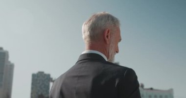 Gri saçlı mali danışman telefonda konuşuyor, sözleşme detaylarını tartışıyor.