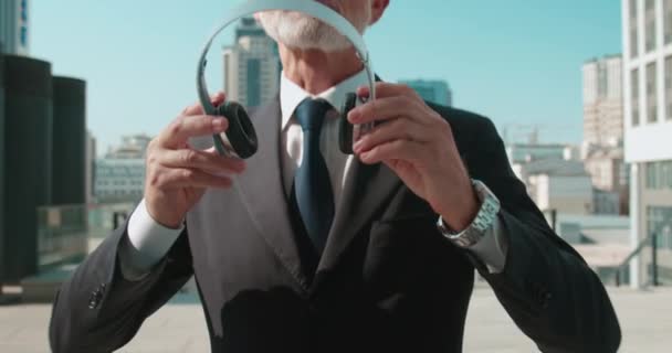 Homme d'affaires aux cheveux gris portant un casque, écoutant sa chanson préférée, amusant — Video