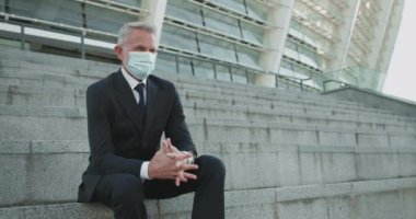 Yüzü maskeli sıkıntılı işadamı merdivenlerde oturuyor, salgın krizinden umudunu kesmiş.