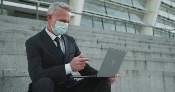 Hombre con máscara que tiene llamada de conferencia en el ordenador portátil en línea, negocio durante la pandemia — Vídeos de Stock