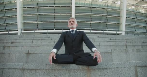 Hombre de negocios tranquilo meditando en las escaleras en posición de loto fijando la mente para el éxito — Vídeo de stock