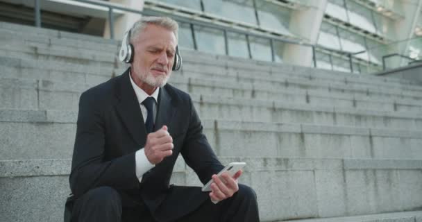 Heureux homme d'affaires senior appréciant la musique préférée dans les écouteurs, se reposer après le travail — Video
