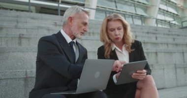 Şirket çalışanları açık hava projesinde birlikte çalışıyorlar. Laptop ve tablet kullanıyorlar.
