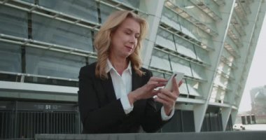 Başarılı iş kadını ofis binası yakınında akıllı telefon kaydırıyor, teknoloji...