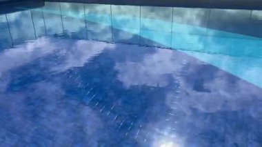 Temiz yüzme havuzu yüzeyi bulutlu mavi gökyüzü ve güneş ışığını yansıtıyor. Huzurlu ve ferahlatıcı bir atmosfer yaratıyor. Rahatlama, tatil, sağlık, spa ve modern yaşam tarzı kavramları için mükemmel.