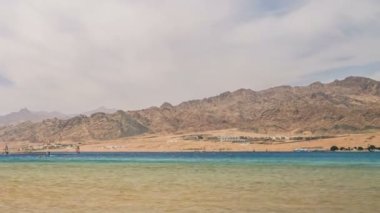 Dağın arka planında, deniz kıyısında yürüyen insanların zamanaşımı 
