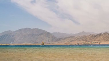 Dağın arka planında, deniz kıyısında yürüyen insanların zamanaşımı 
