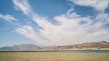 Dağın arka planında, deniz kıyısında yürüyen insanların zamanaşımı 