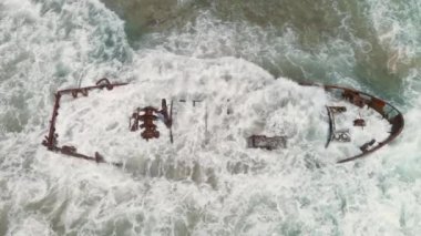 İsrail 'deki Ha Bonim plajında paslı bir gemi enkazına çarpan dalgalar, hava aracı görüntüsü, 4K ağır çekim.