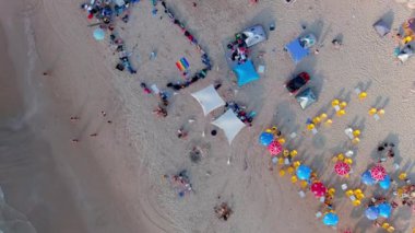 Gemi enkazı, renkli çadırları ve şemsiyeleri olan resimli bir yaz plajı.