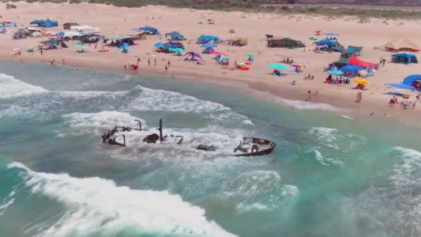 難破船やカラフルなテントや傘 空中ドローントップダウンビューで絵のような夏のビーチ4K — ストック動画