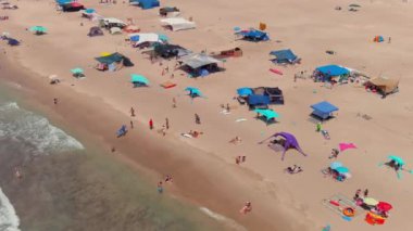 Gemi enkazı, renkli çadırları ve şemsiyeleri olan resimli bir yaz plajı.