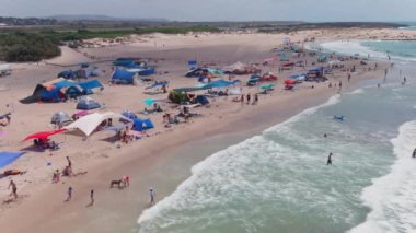 Gemi enkazı, renkli çadırları ve şemsiyeleri olan resimli bir yaz plajı.