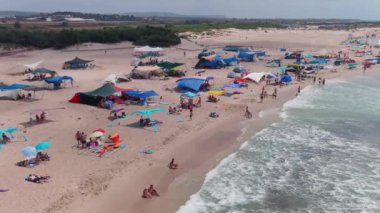Gemi enkazı, renkli çadırları ve şemsiyeleri olan resimli bir yaz plajı.