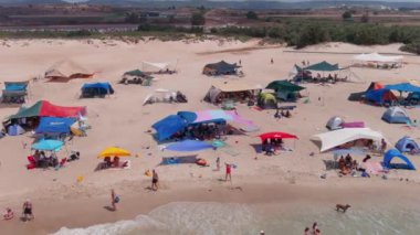 Gemi enkazı, renkli çadırları ve şemsiyeleri olan resimli bir yaz plajı.