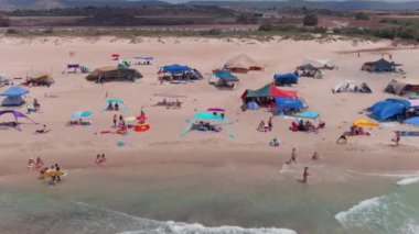 Gemi enkazı, renkli çadırları ve şemsiyeleri olan resimli bir yaz plajı.