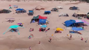 Gemi enkazı, renkli çadırları ve şemsiyeleri olan resimli bir yaz plajı.