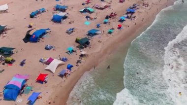 Gemi enkazı, renkli çadırları ve şemsiyeleri olan resimli bir yaz plajı.