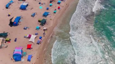 Gemi enkazı, renkli çadırları ve şemsiyeleri olan resimli bir yaz plajı.