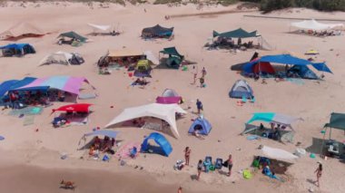 Gemi enkazı, renkli çadırları ve şemsiyeleri olan resimli bir yaz plajı.