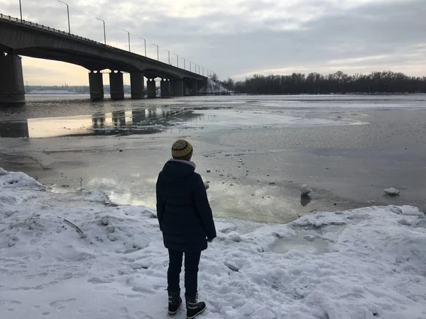 Kadın köprünün yanındaki donmuş nehrin karşı gökyüzü ve bulutlar üzerinde günbatımında duruyor.