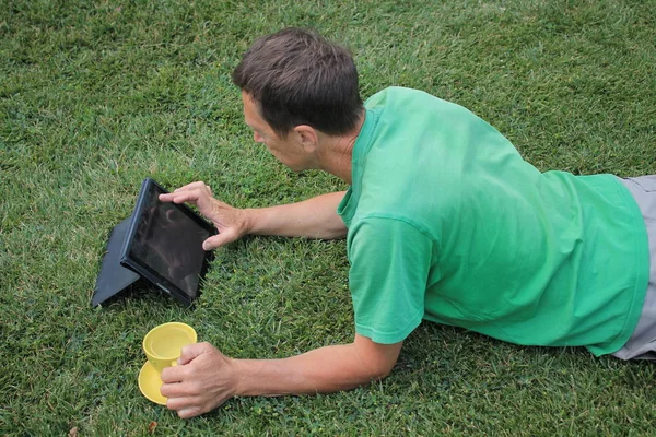 Mężczyzna w średnim wieku leży na trawniku i patrzy w komputerze typu Tablet. — Zdjęcie stockowe