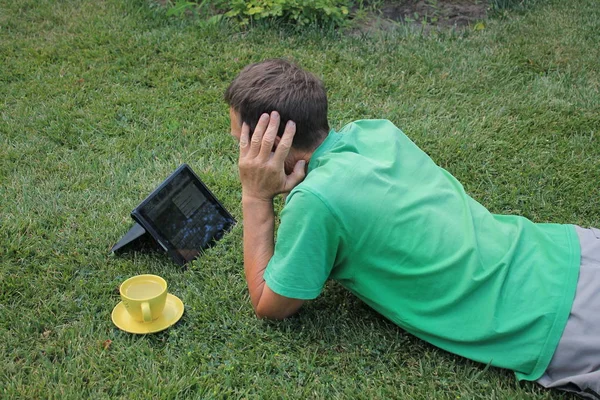 Orta yaşlı bir adam çimenlikte yatıyor ve tablet bilgisayara bakıyor..