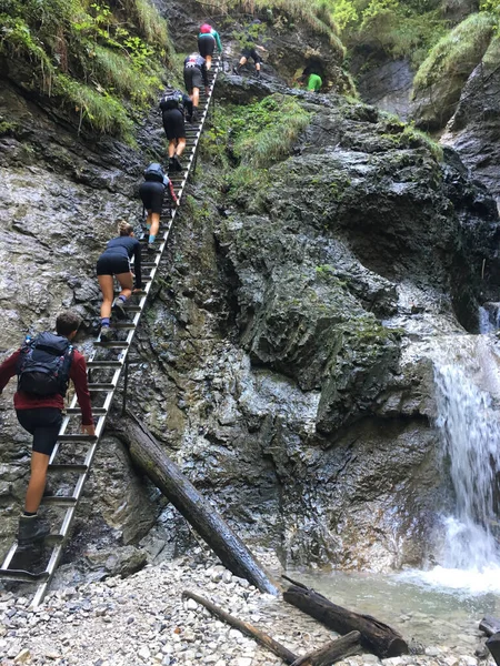 Hikers with backpacks climb stairs up to the gorge near waterfall in Slovak Paradise park.