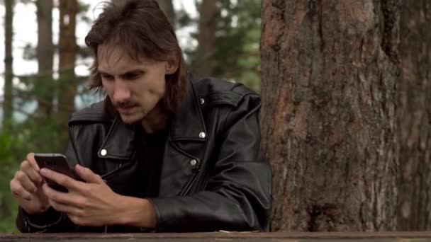 Парень сидит с телефоном в лесу — стоковое видео