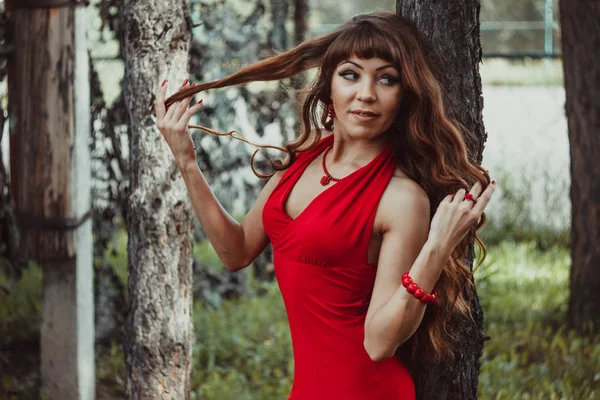 Dívka s dlouhé a vlnité vlasy v červených šatech v lese — Stock fotografie