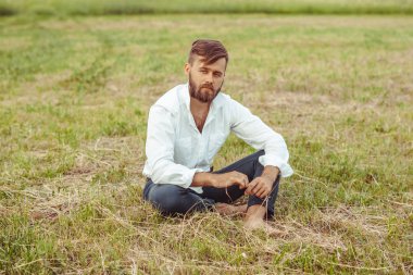 çimenlerin üzerinde oturan sakallı adam