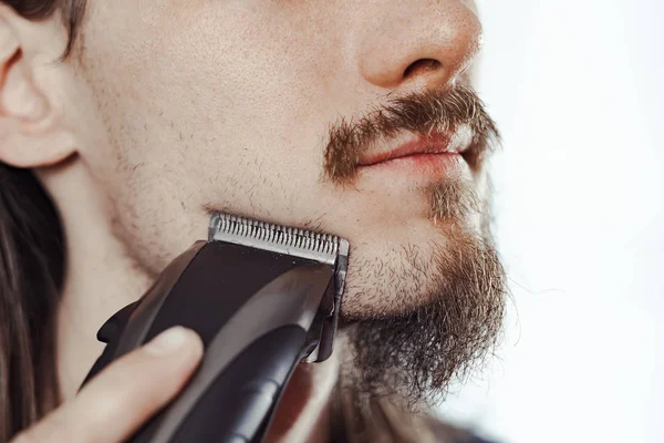 Guy shaves his beard with an electric razor — Stock Photo, Image