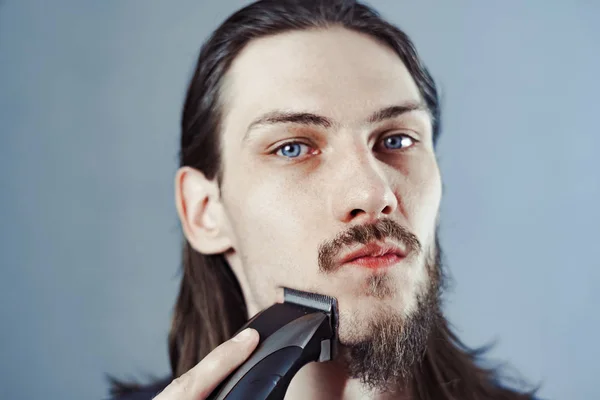 Guy shaves his beard with an electric razor — Stock Photo, Image