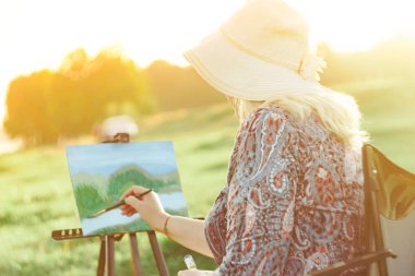 yaşlı bir kadın doğada bir resim boyar