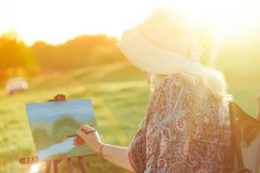 yaşlı bir kadın doğada bir resim boyar