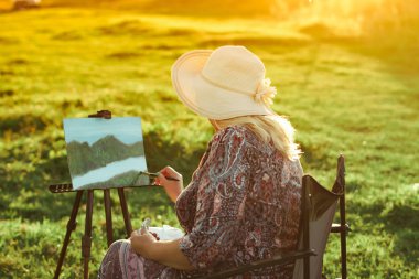 yaşlı bir kadın doğada bir resim boyar